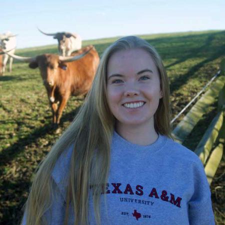 Zoe Halpate showing she is going to Texas A&M in front of a field of longhorn cows