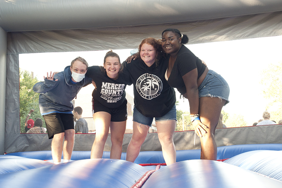 Four students in shorts bend over for a photo in an air-filled bounce castle