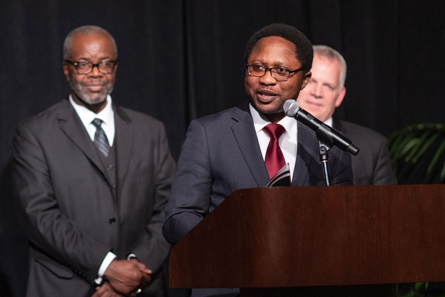 A man in a suit speaks at a podium while holding an award