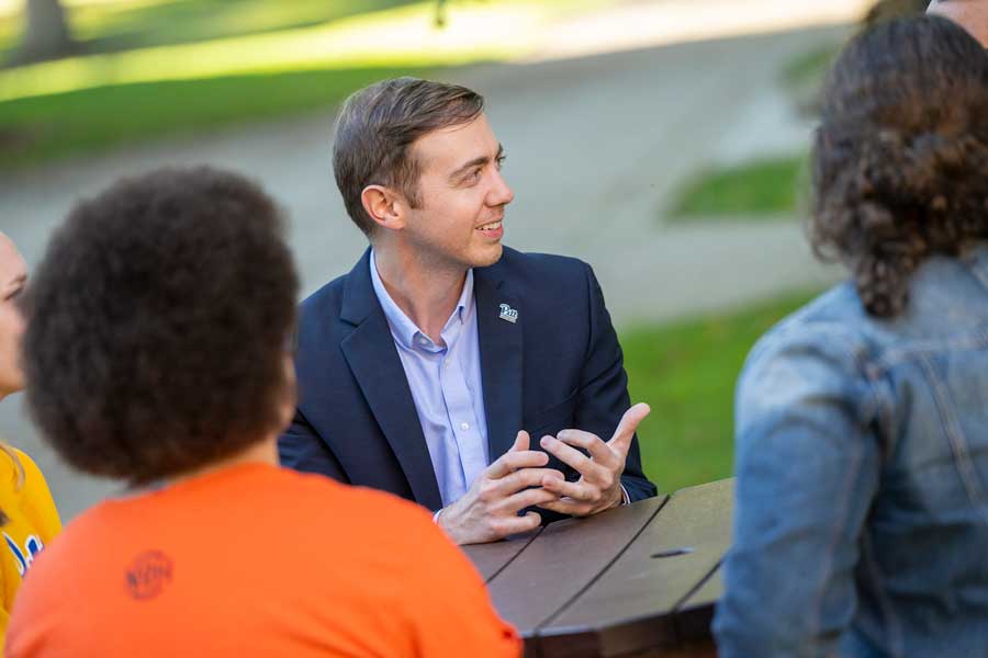 Dr. Dean Davila sitting at a picnic bench in the summer with other students