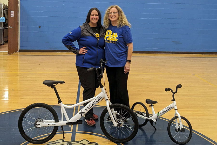 Two faculty standing behind Strider bikes