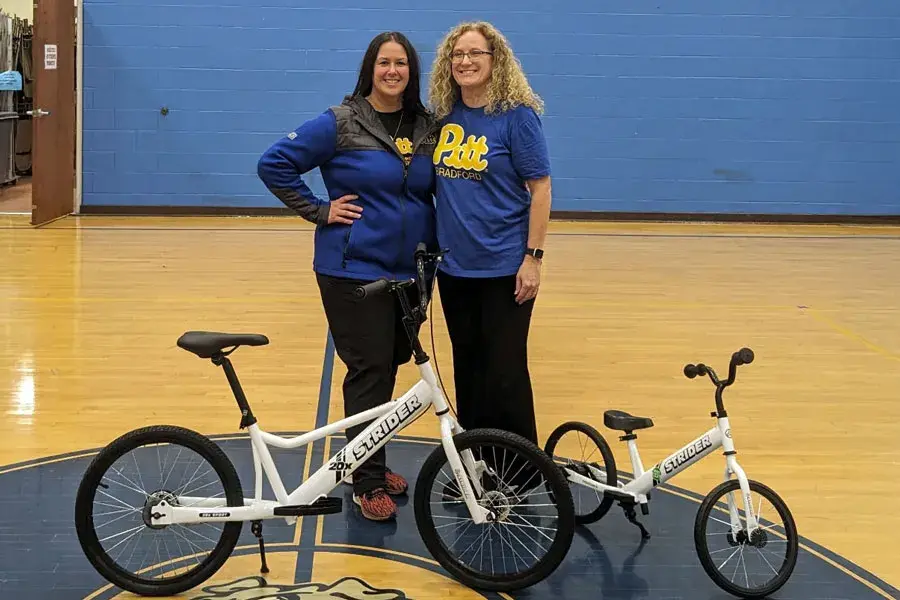 Two faculty standing behind Strider bikes