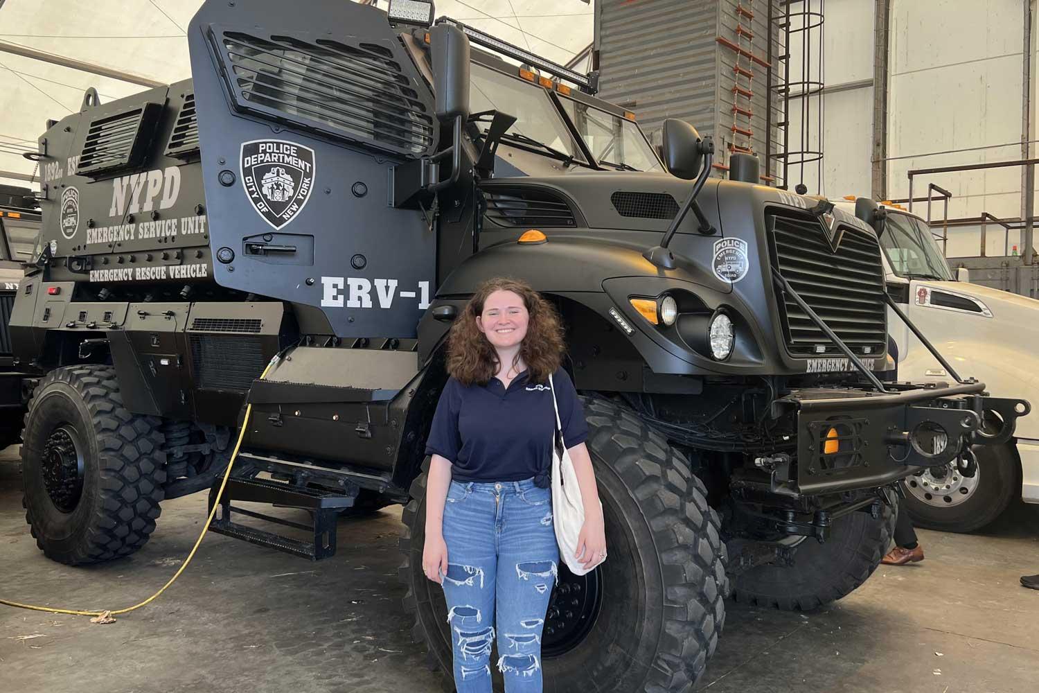 Emma Weir standing in front of an armored vehicle.