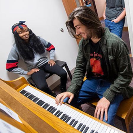 A male and female student at a piano in a practice room