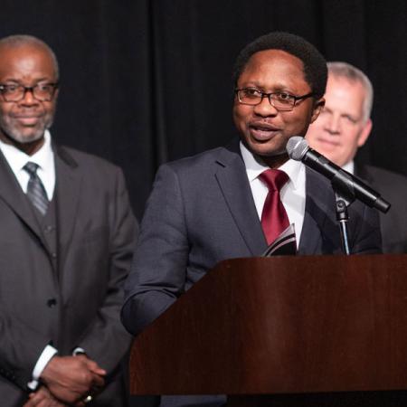 A man in a suit speaks at a podium while holding an award