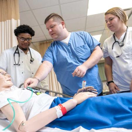 Photo of students with a professor practicing nursing exercises on a dummy