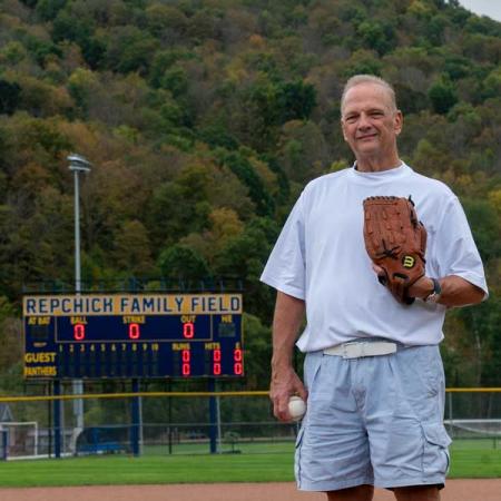 George Repchick standing at the pitcher's mound with the dedicated scoreboard behind him