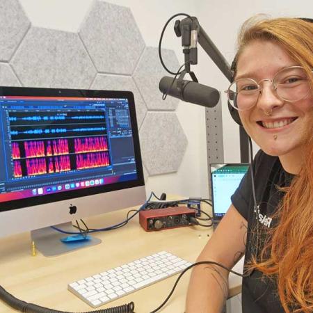 Hayley sitting at a desk with a omputer screen and microphone.