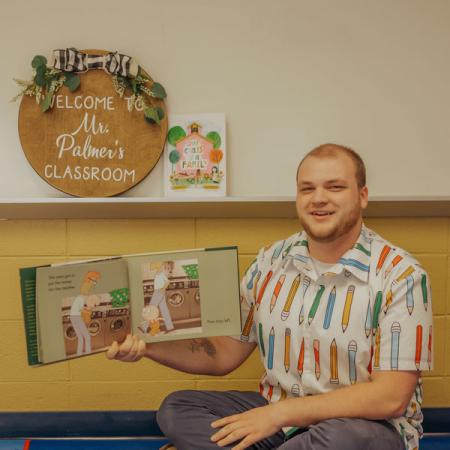 Cole reading holding a bok with stuffed animals in the foreground