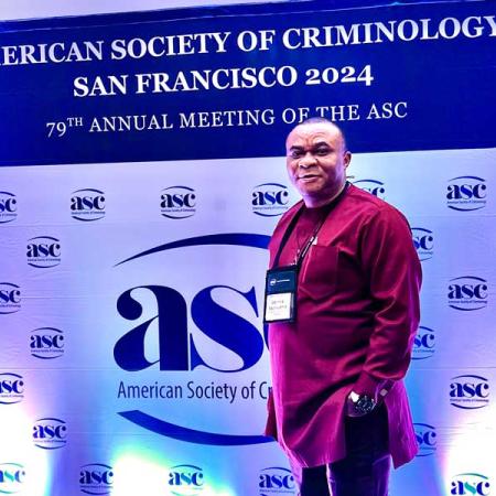 Dr. Obinna Ezeihuoma in front of a backdrop for the American Society of Criminology