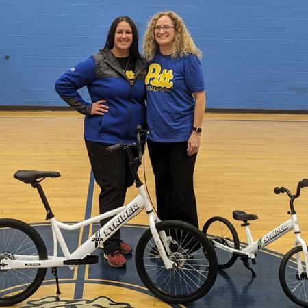 Two faculty standing behind Strider bikes