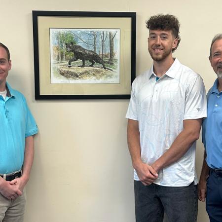 Chris and Gus Napoleon standing with Mychal Berlinski in front of a portrait of the panther statue